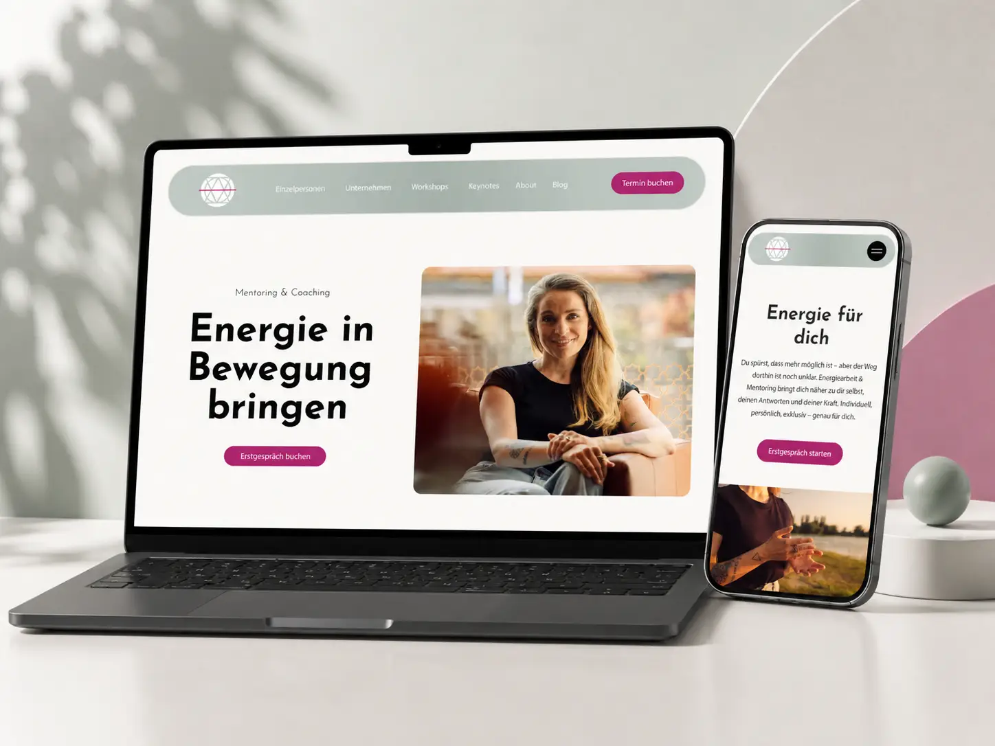 Ein Laptop und ein Smartphone zeigen eine Coaching-Website mit dem Foto einer lächelnden Frau, dem Text "Energie in Bewegung bringen" und Schaltflächen zur Buchung eines Beratungstermins. Die Geräte stehen auf einem hellen Schreibtisch mit sanftem Tageslicht. fotograf-webdesigner-seo-agentur-hochzeitsfotograf-abgelichtet